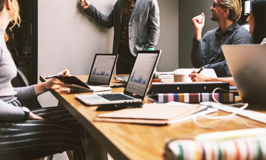 A group of professionals in a meeting, discussing strategies around a table with laptops displaying data charts. This scene reflects a collaborative environment in digital marketing agencies near me, where teams analyze data to optimize campaigns.